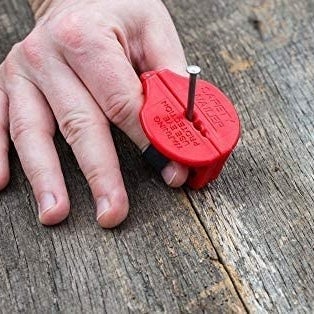 A hand with the small red gadget pinched between thumb and pointer finger