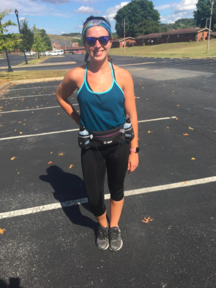 Reviewer wears black and purple hydration running belt with black capri leggings, a blue tank top, and gray running sneakers