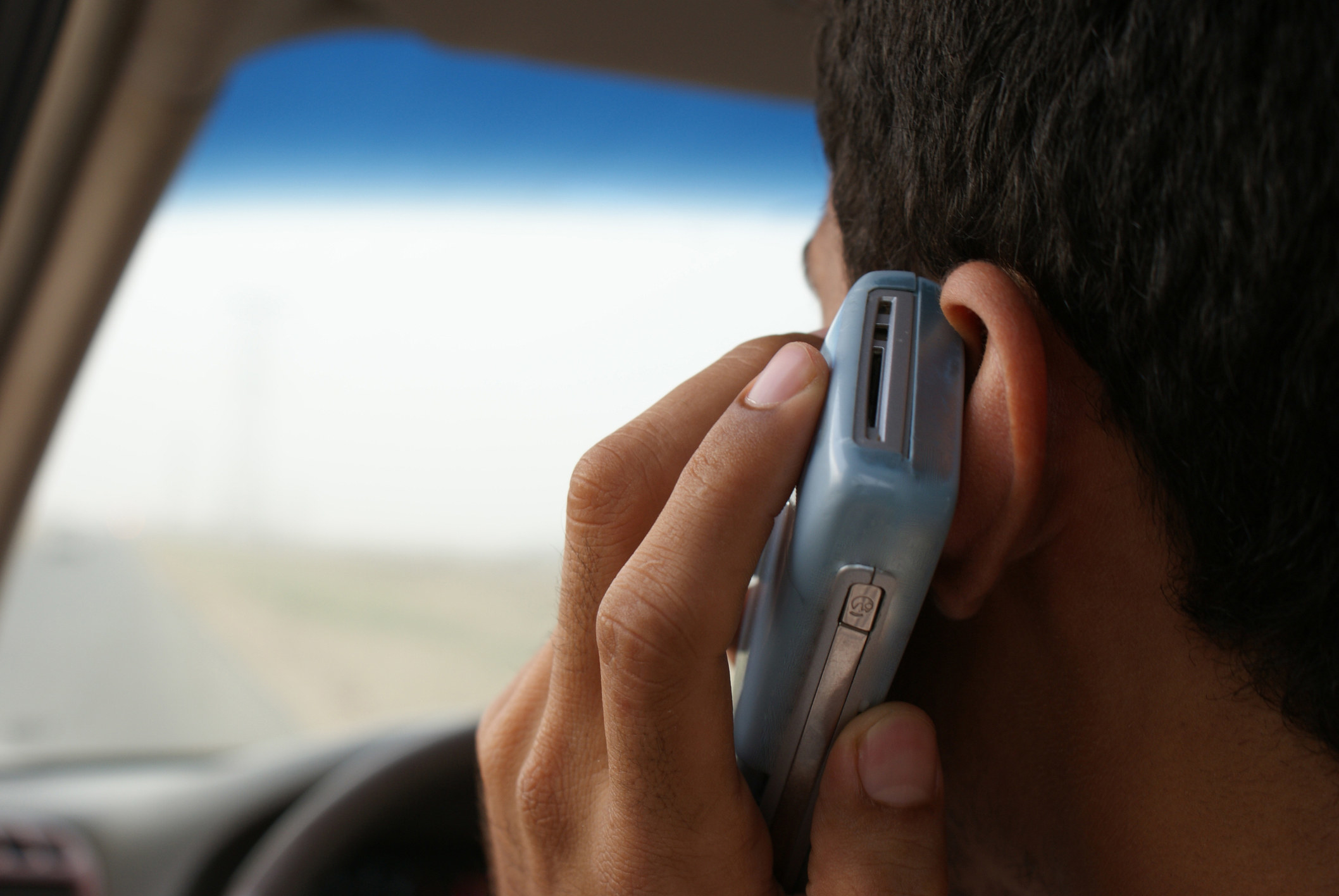 A stock image of a teen sitting in a car with phone up to his ear