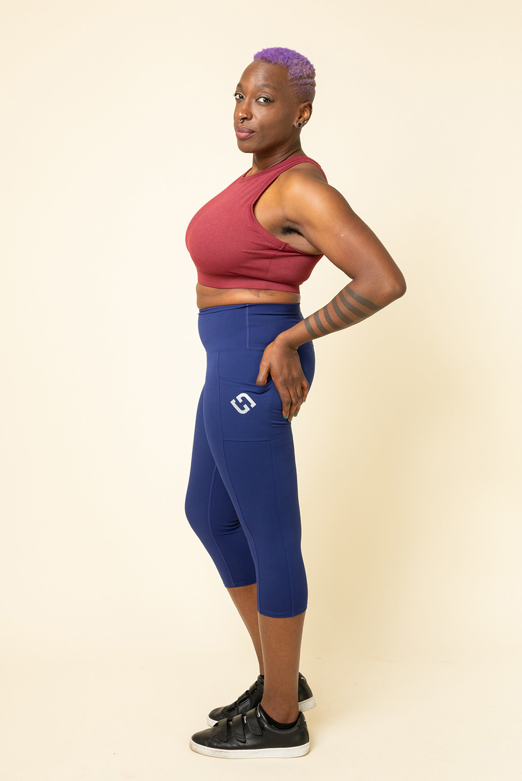 Model wears dark blue capris with a red crop top and black sneakers