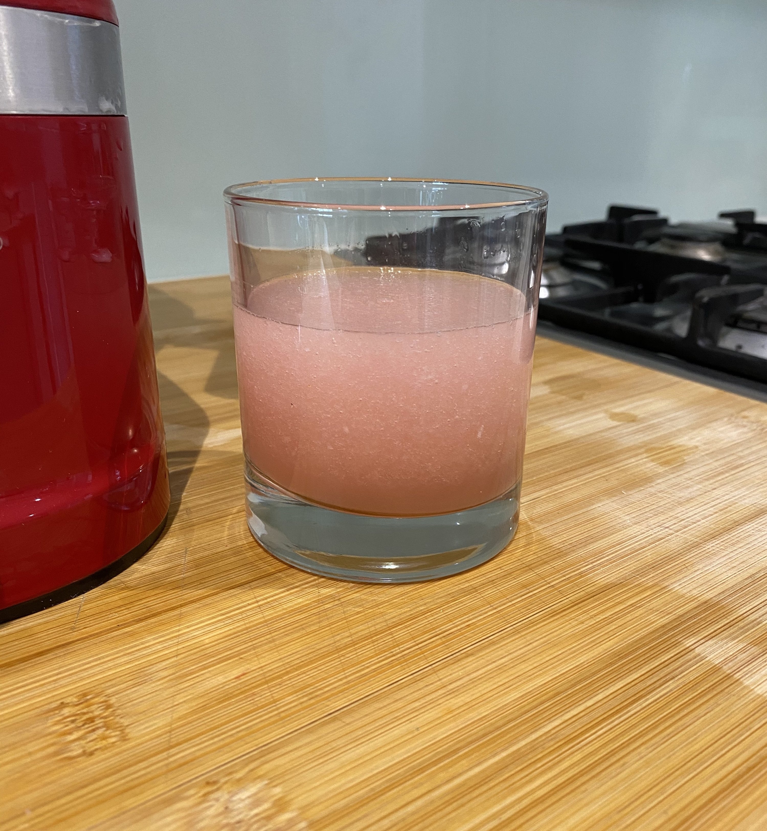 A short glass filled with a pink slushy standing next to a blender