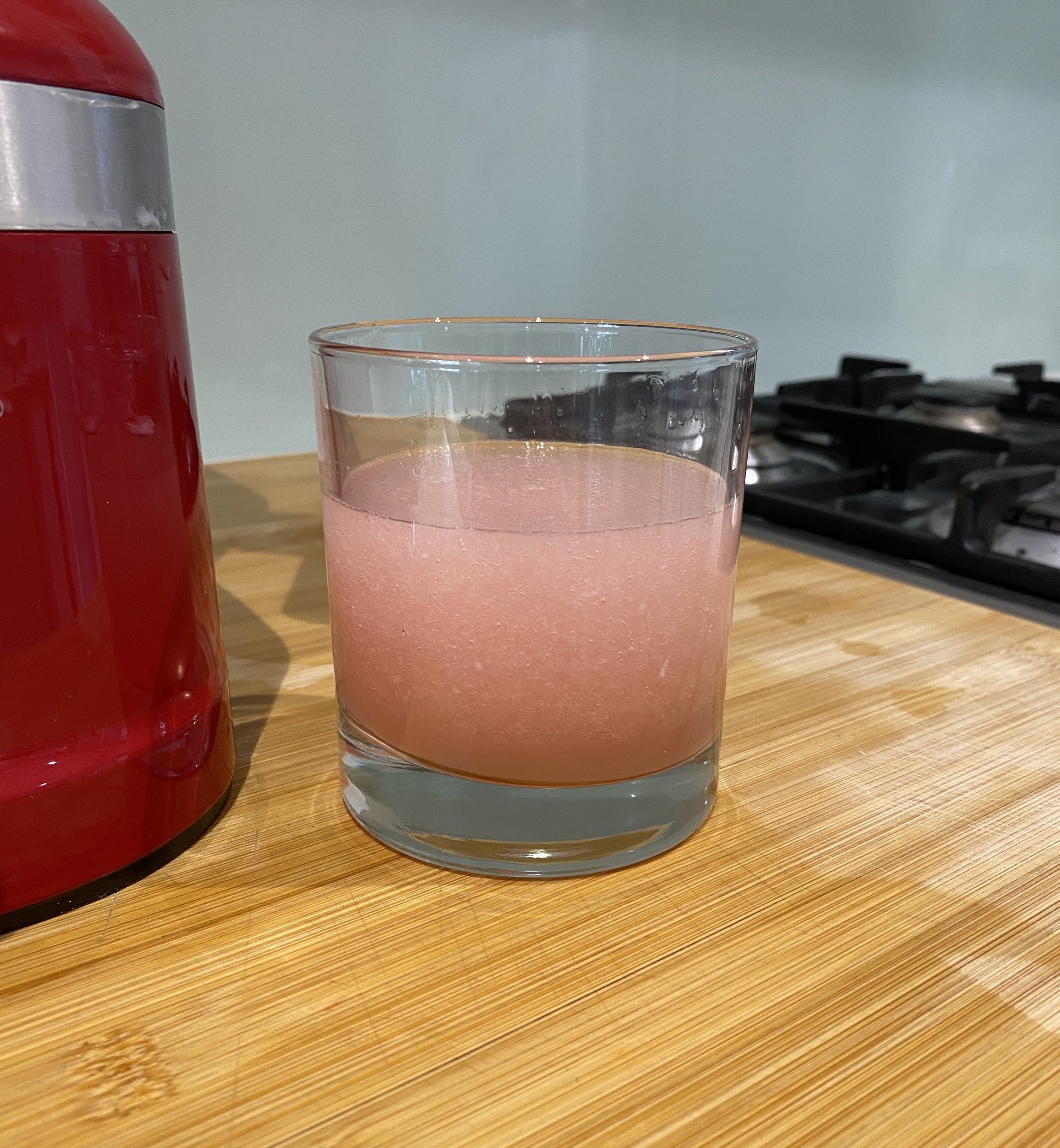 A short glass filled with a pink slushy standing next to a blender