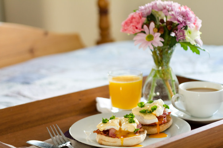 Breakfast in bed with eggs benedict, hollandaise sauce, OJ, coffee and some flowers 