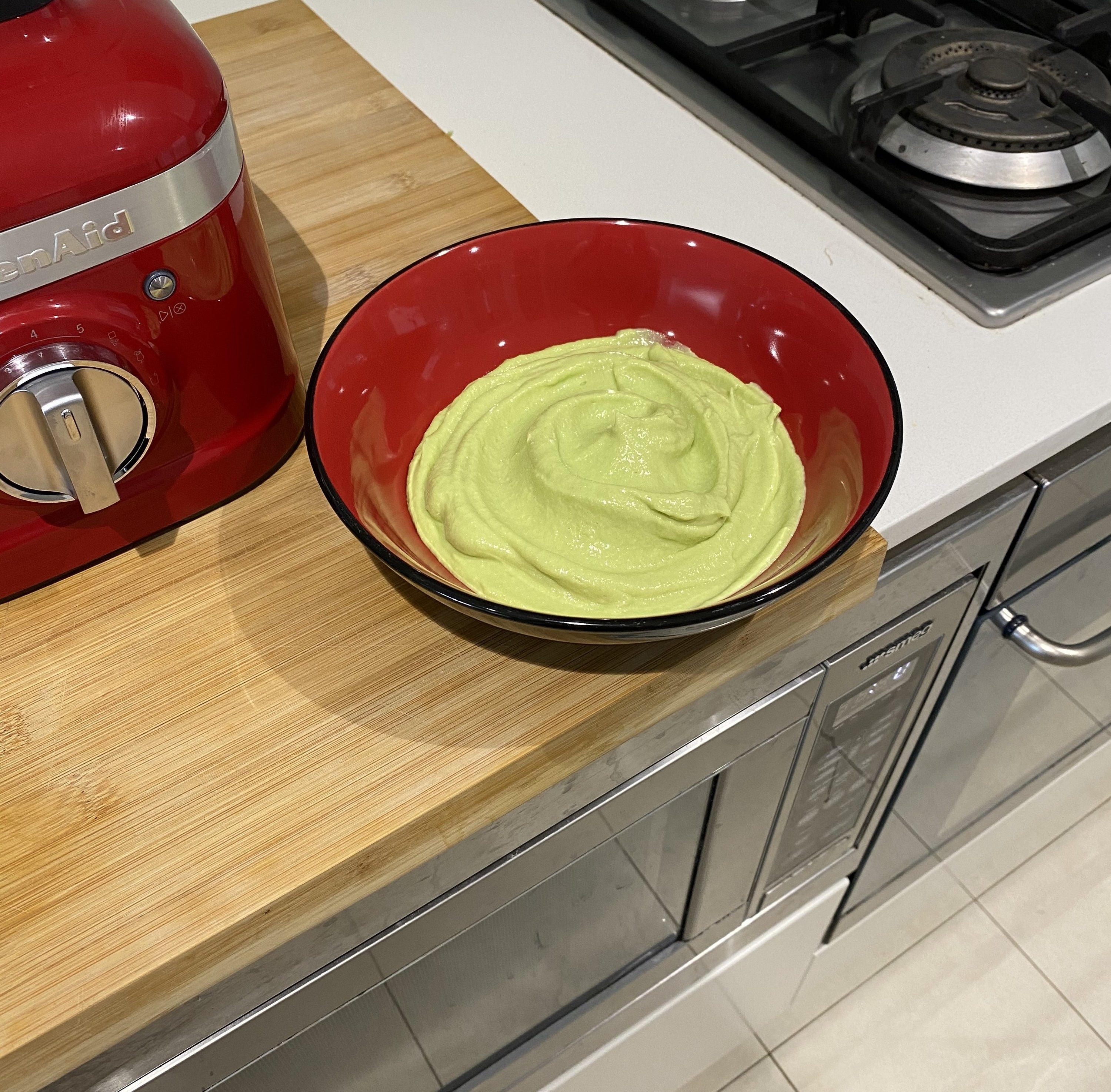 A bowl of smooth guacamole sitting on a bench next to a blender