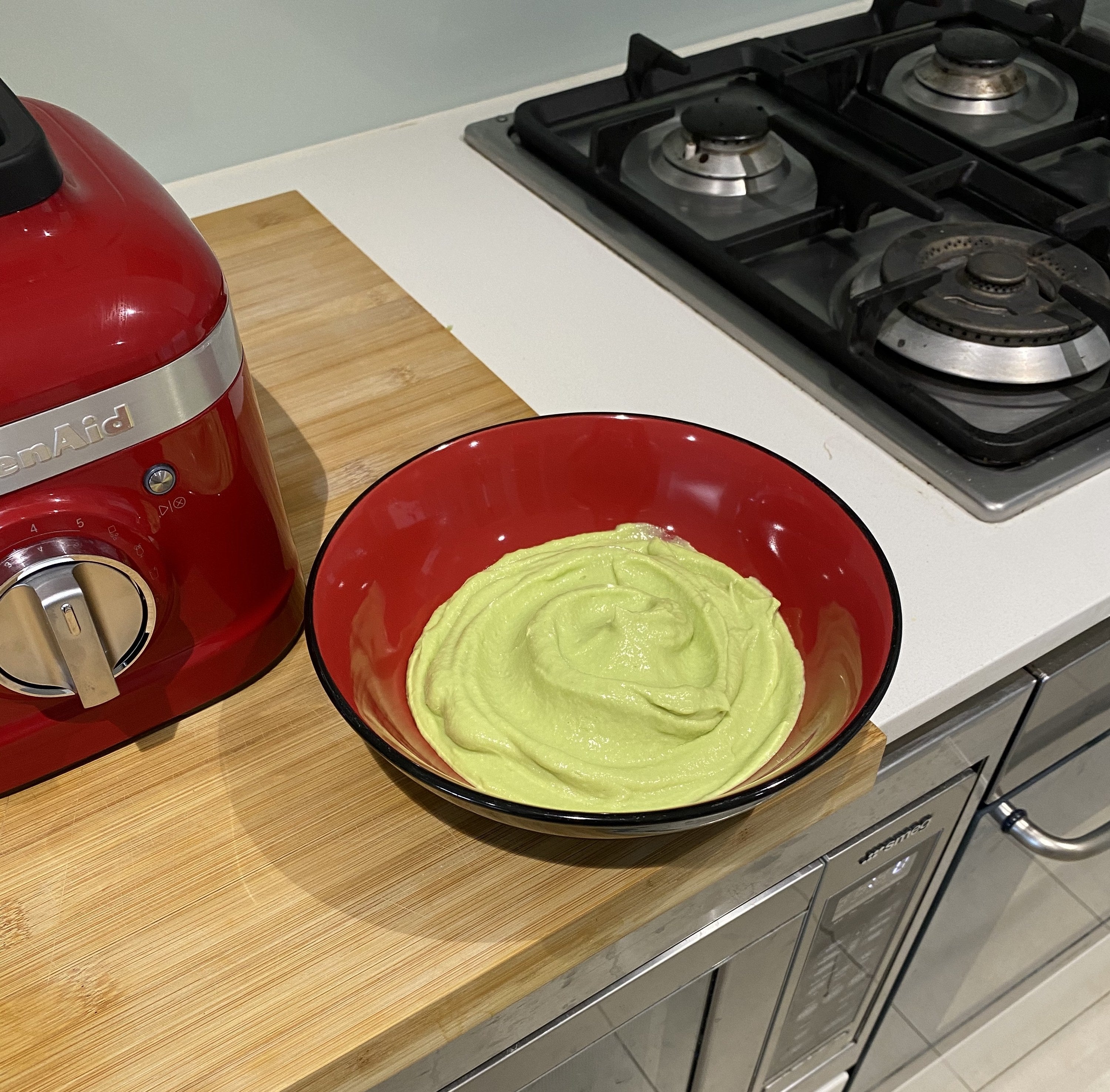 A bowl of smooth guacamole sitting on a bench next to a blender