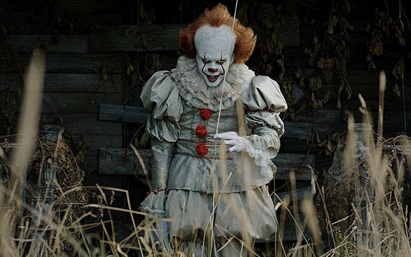 Pennywise the scary clown holding a balloon and smiling wickedly