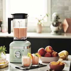 Pastel green KitchenAid blender half full and sitting in a kitchen next to fresh peaches