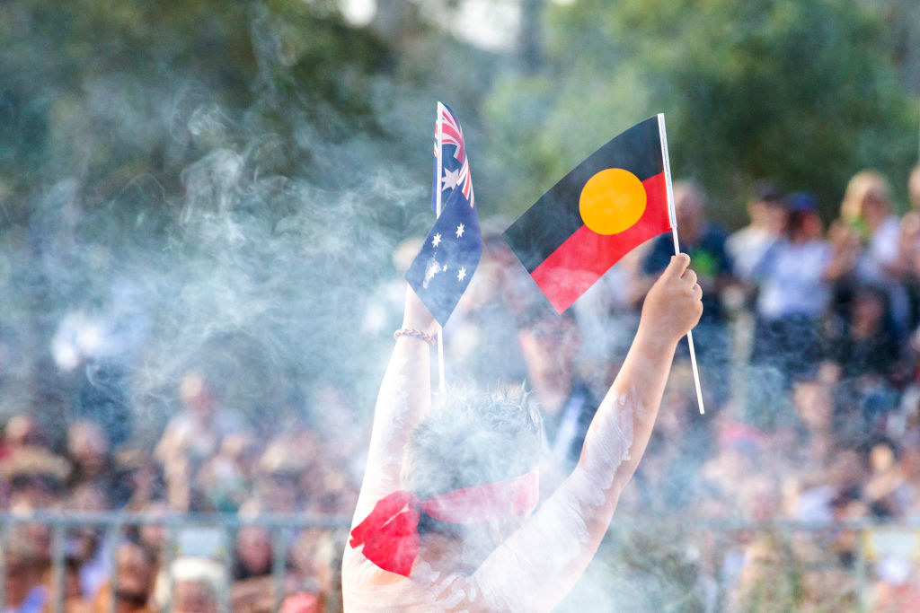 A First Nations person holding up the Australian and Aboriginal flag