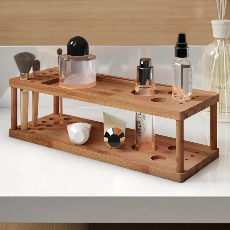 A freestanding bamboo makeup organizer with two shelves and a variety of differently sized holes