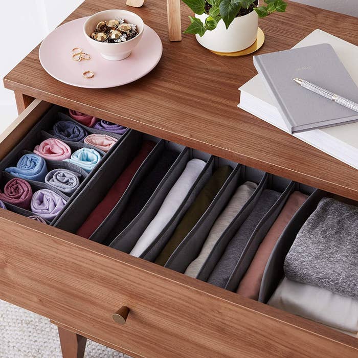 Gray cloth organizers inside an open drawer filled with socks and other clothes