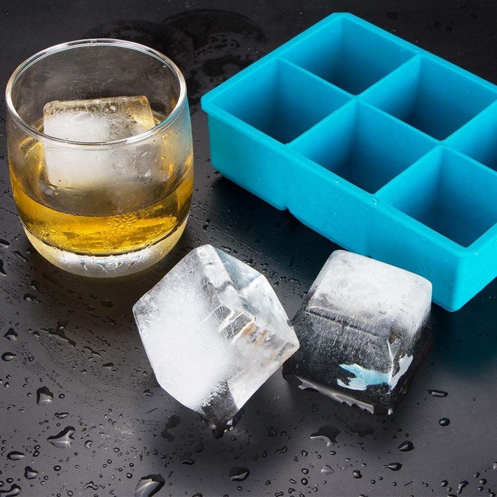 The ice cube tray next to two cubes and a cocktail