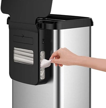 The back of the GLAD Extra Capacity Stainless Steel Sensor Trash Can where a model pulls a garbage bag out of the rear holder