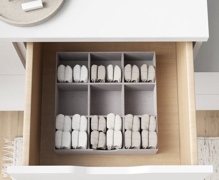 The gray organizer inside of a drawer with folded garments inside of it