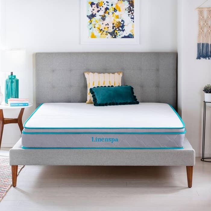 A light gray mattress with teal-colored piping and logo
