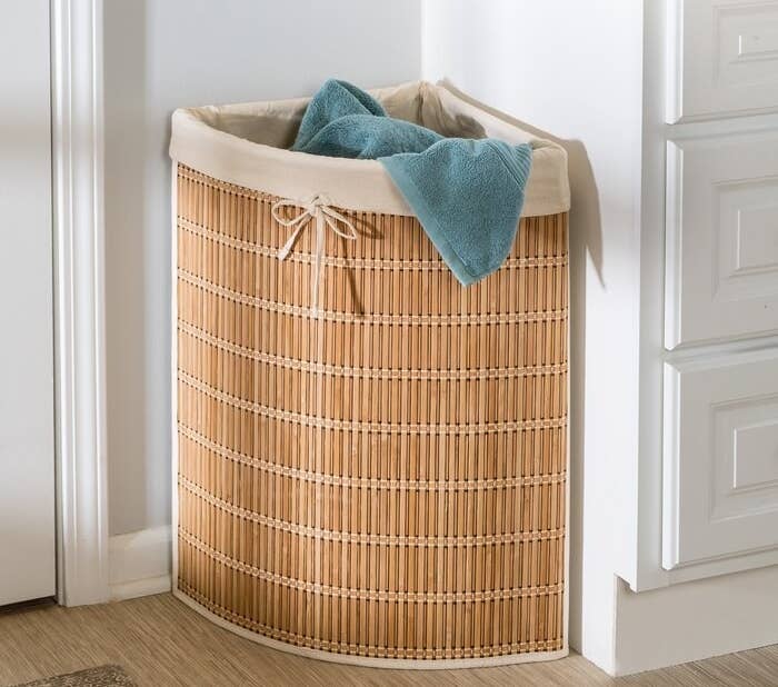 The tan colored wicker hamper against the corner of a wall filled with laundry