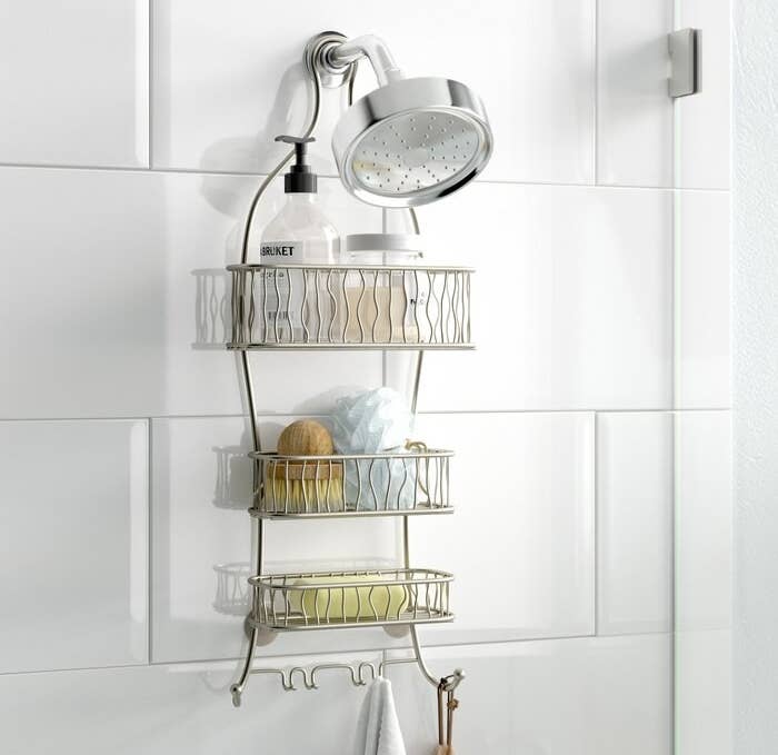 The silver shower caddy hanging over the shower head holding various shower products