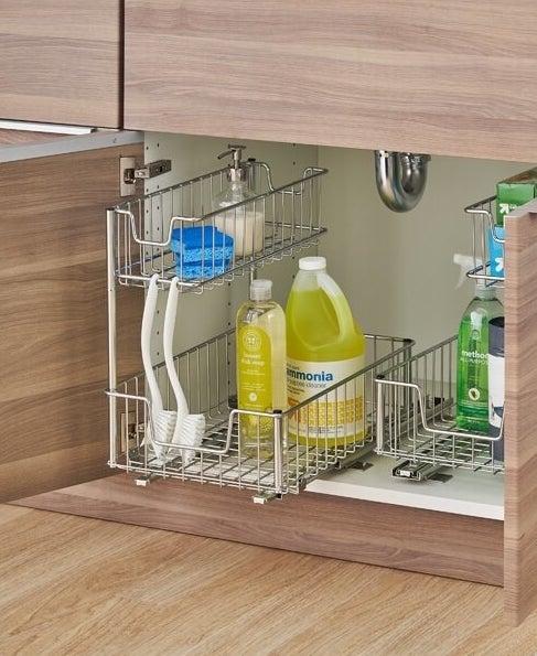 The under-the-sink pull-out organizer holding various cleaning products, sponges, scrub brushes, and plastic bag boxes