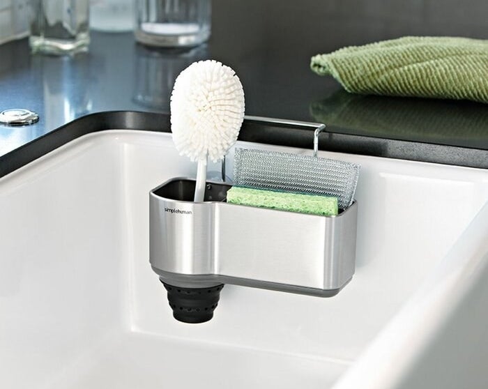 A shower caddy attached to a sink holding a sponge and a scrubbing brush