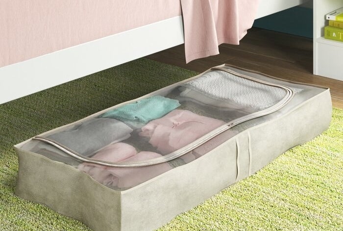 The storage bags organizer pulled out from underneath a bed with folded clothing inside