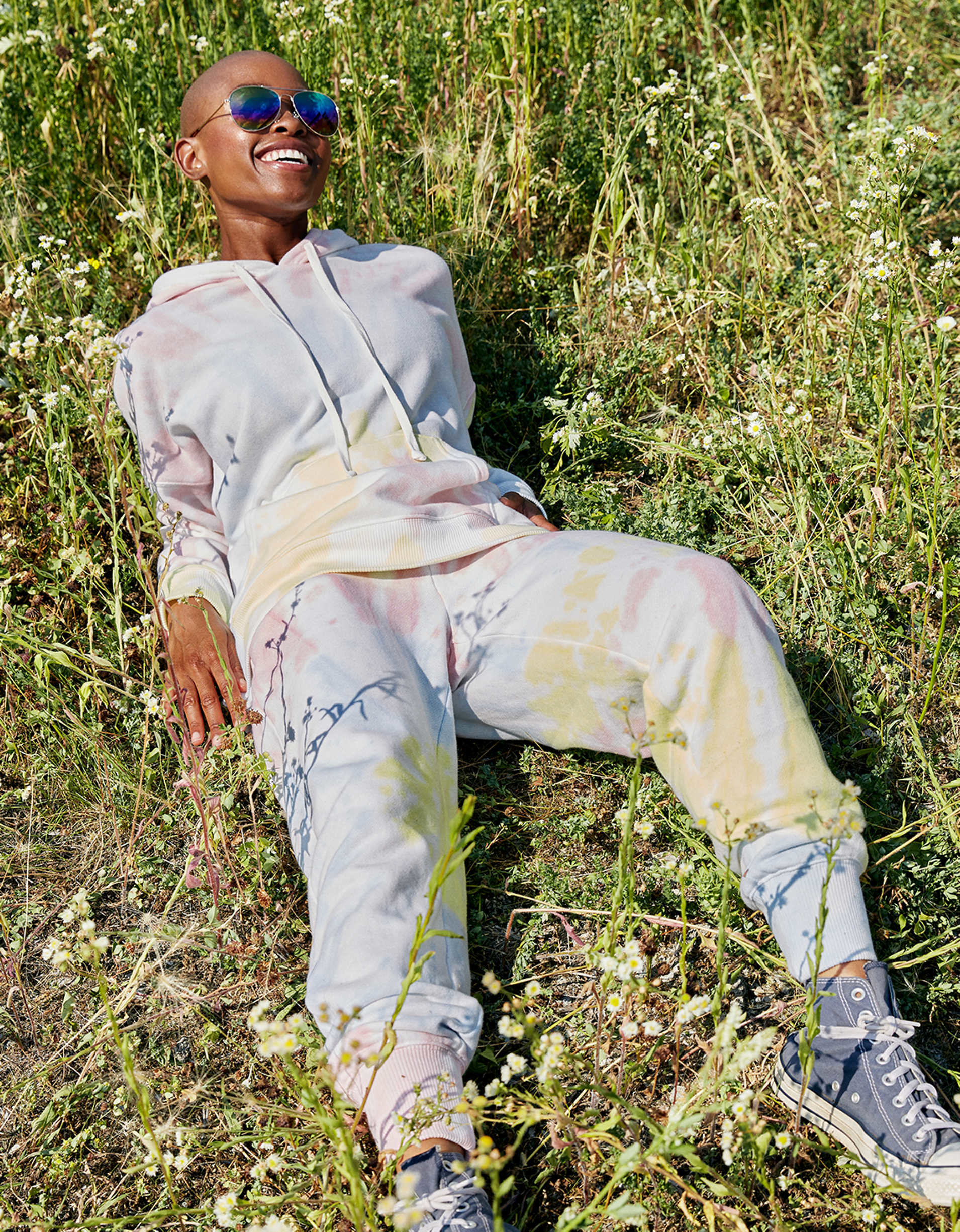 Model wearing the hooded sweatshirt and sweatpants with a muted pink, yellow, and blue tie-dye pattern on both