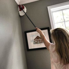 A person uses the mop to reach into a high ceiling corner