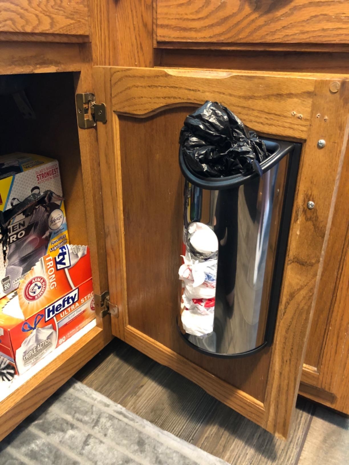 A stainless steel and black plastic bag dispenser mounted inside a kitchen cabinet