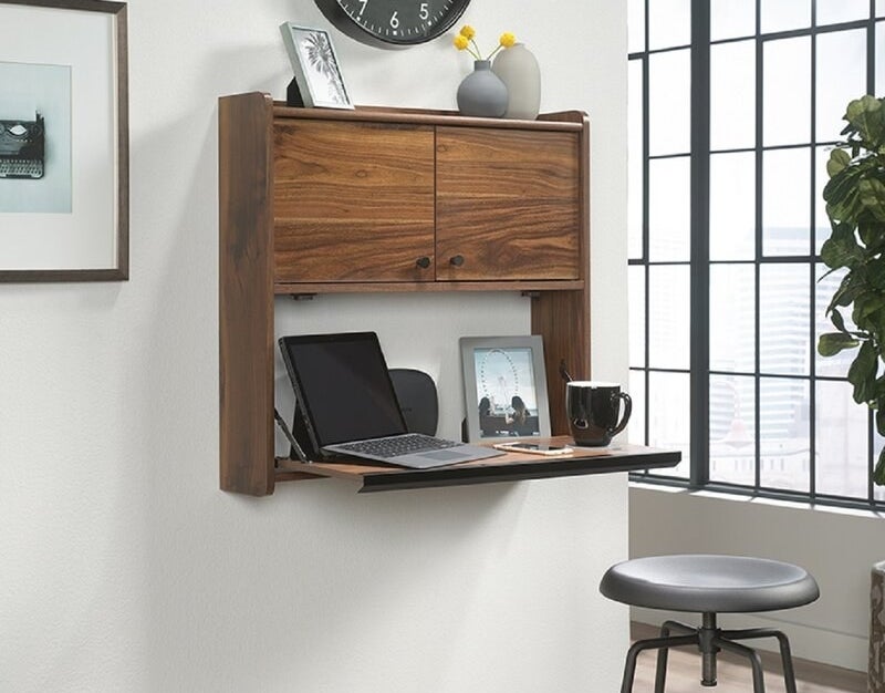 A dark wooden, floating desk holding a computer, a photo, and a cup of coffee on the work surface as well as a photo and vases on the top