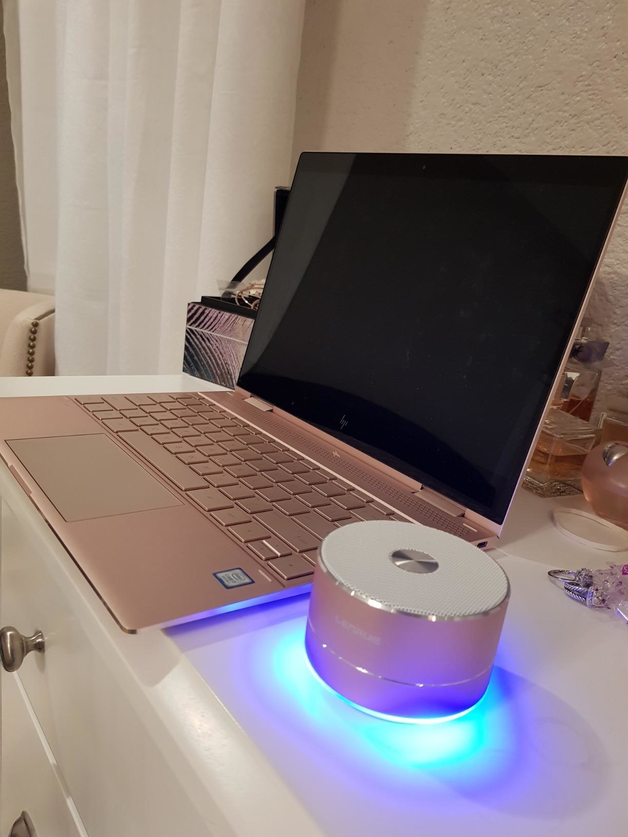 A reviewer showing the small circular speaker next to a laptop
