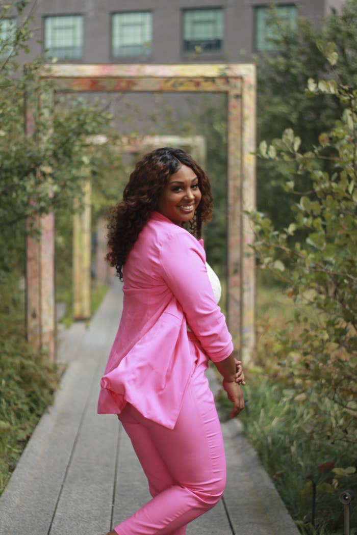 Lyana Blount, owner of Black Rican Vegan wearing a pink suit smiling while she is looking back at the camera in a garden