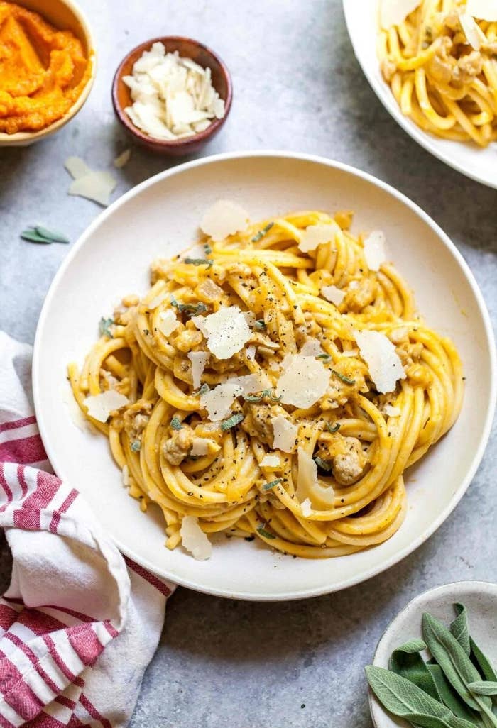 A plate of bucatini in a creamy pumpkin sauce with turkey sausage, parmesan cheese, and fresh sage on the side.