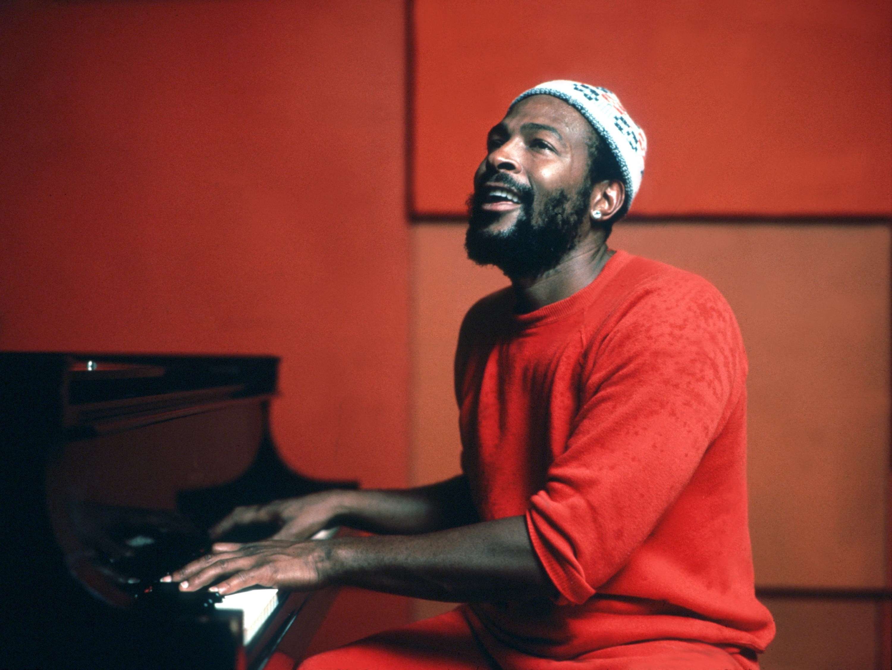 A classic photo Marvin Gaye playing the piano while wearing in orange sweater and in an orange room in 1974