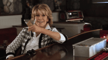 A GIF from &quot;Grace and Frankie&quot; of Jane toasting with a martini while sitting at bar 