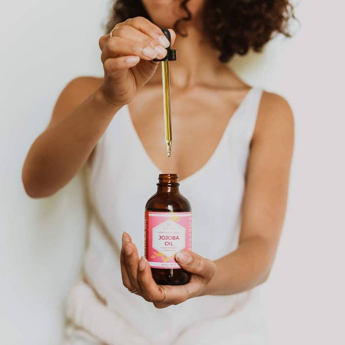 A person holds a bottle of jojoba oil