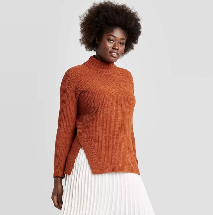Model is wearing a burnt orange mock neck pullover sweater 