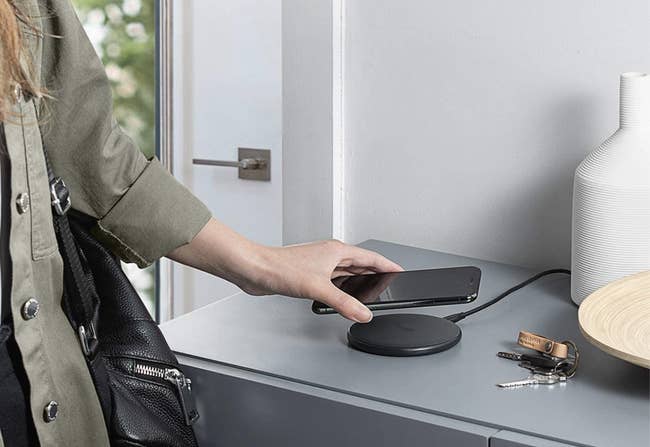 A model placing a phone down on a wireless black charging pad 