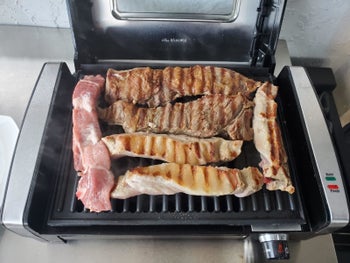 A reviewer showing the grill with meat on it