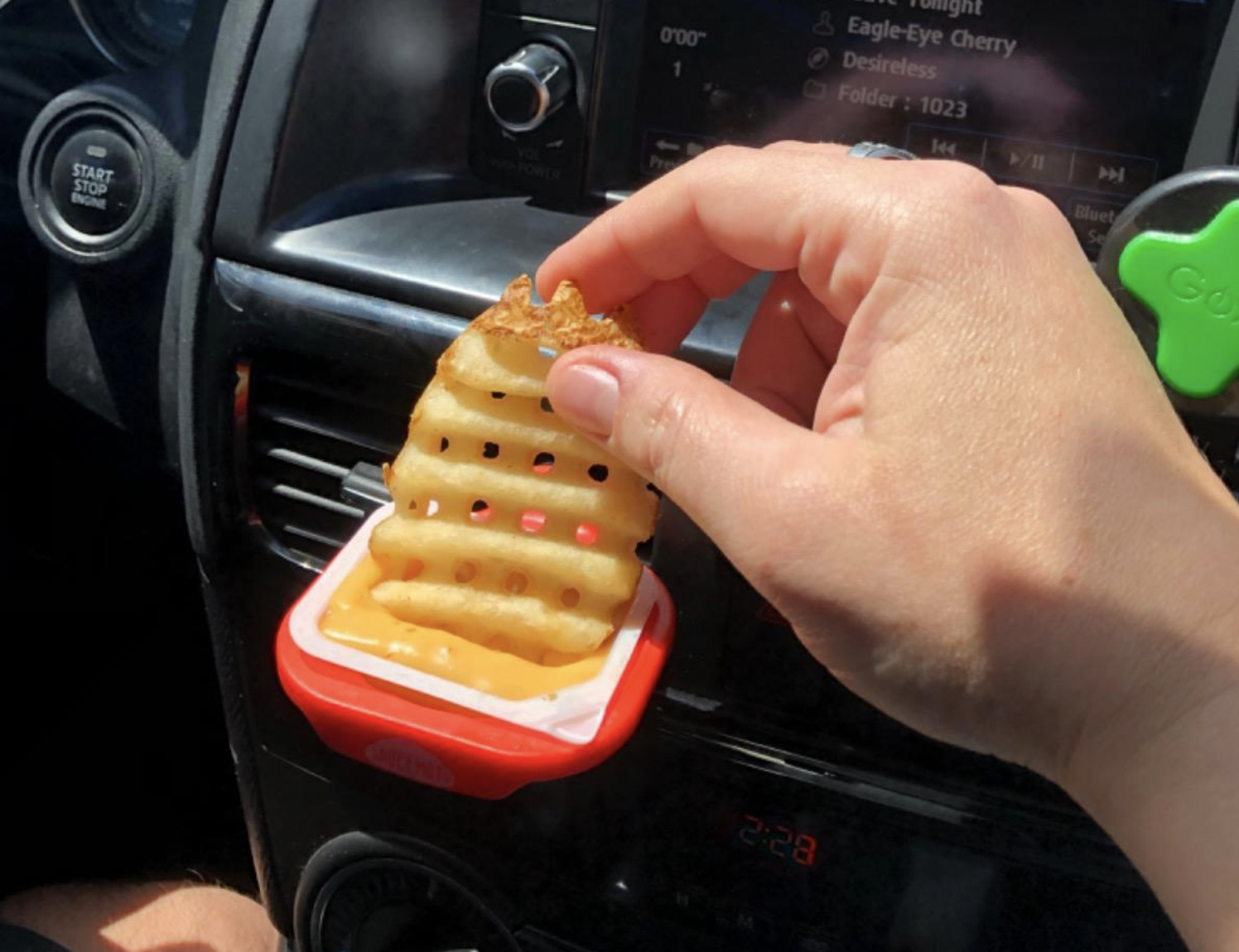 Reviewer dipping a fry into sauce that&#x27;s being help up by the vent clip (that&#x27;s been attached to the car vent)