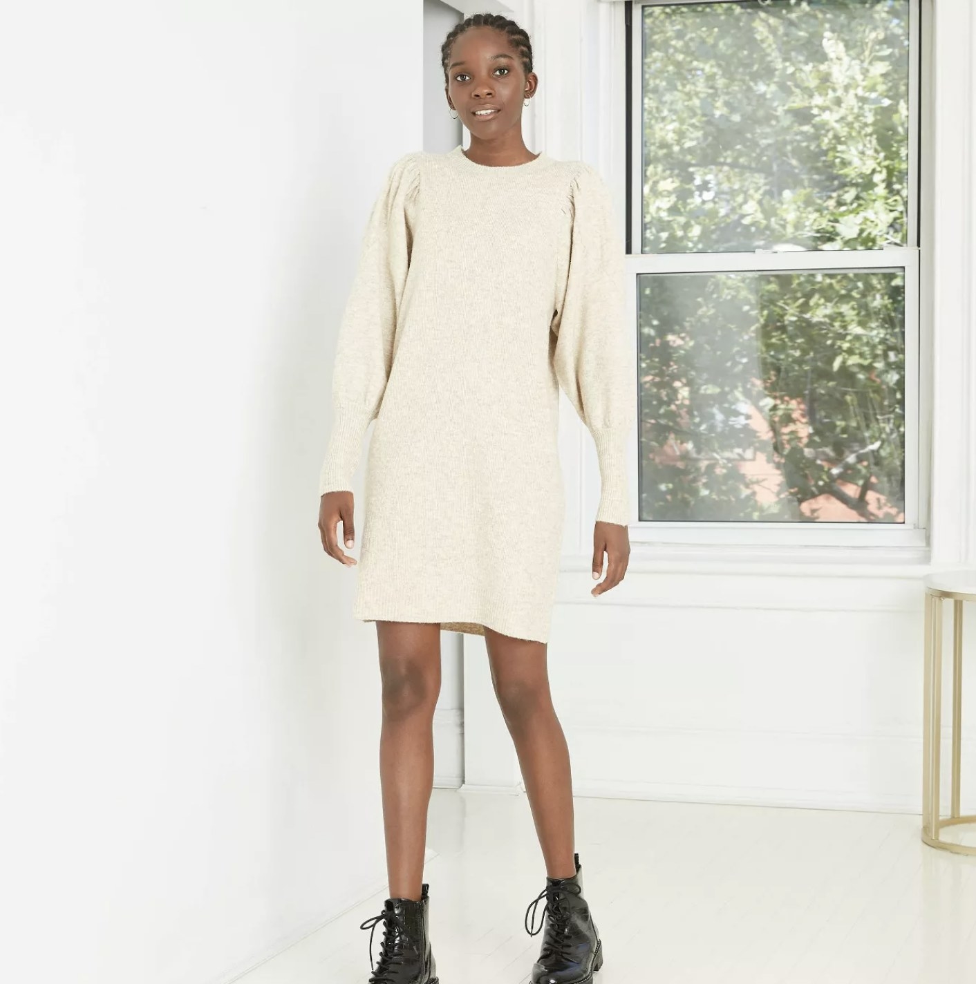 Model is wearing a cream sweater dress with puffed long sleeves