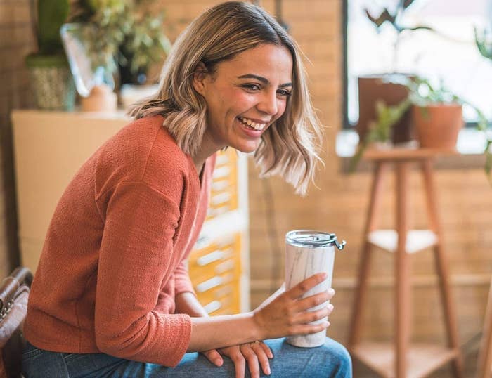 A smiling person holds the tumbler on their lap