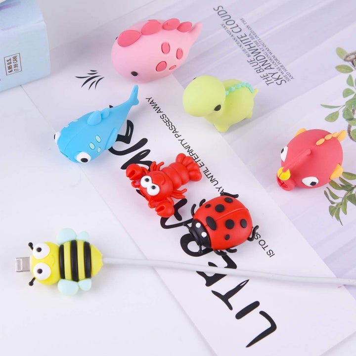 six cable bites sitting on a desk with one shaped like a  bumblebee on sticking on the end of a phone charger