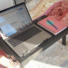 Same laptop tray no longer sitting flat. Instead, it's legs are folded out so it's sitting up about a half-foot off of the bed.