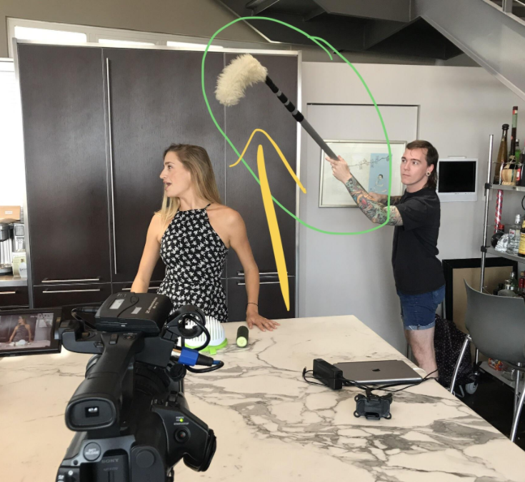 A man holds a long duster over a TV presenter&#x27;s head as she is filmed