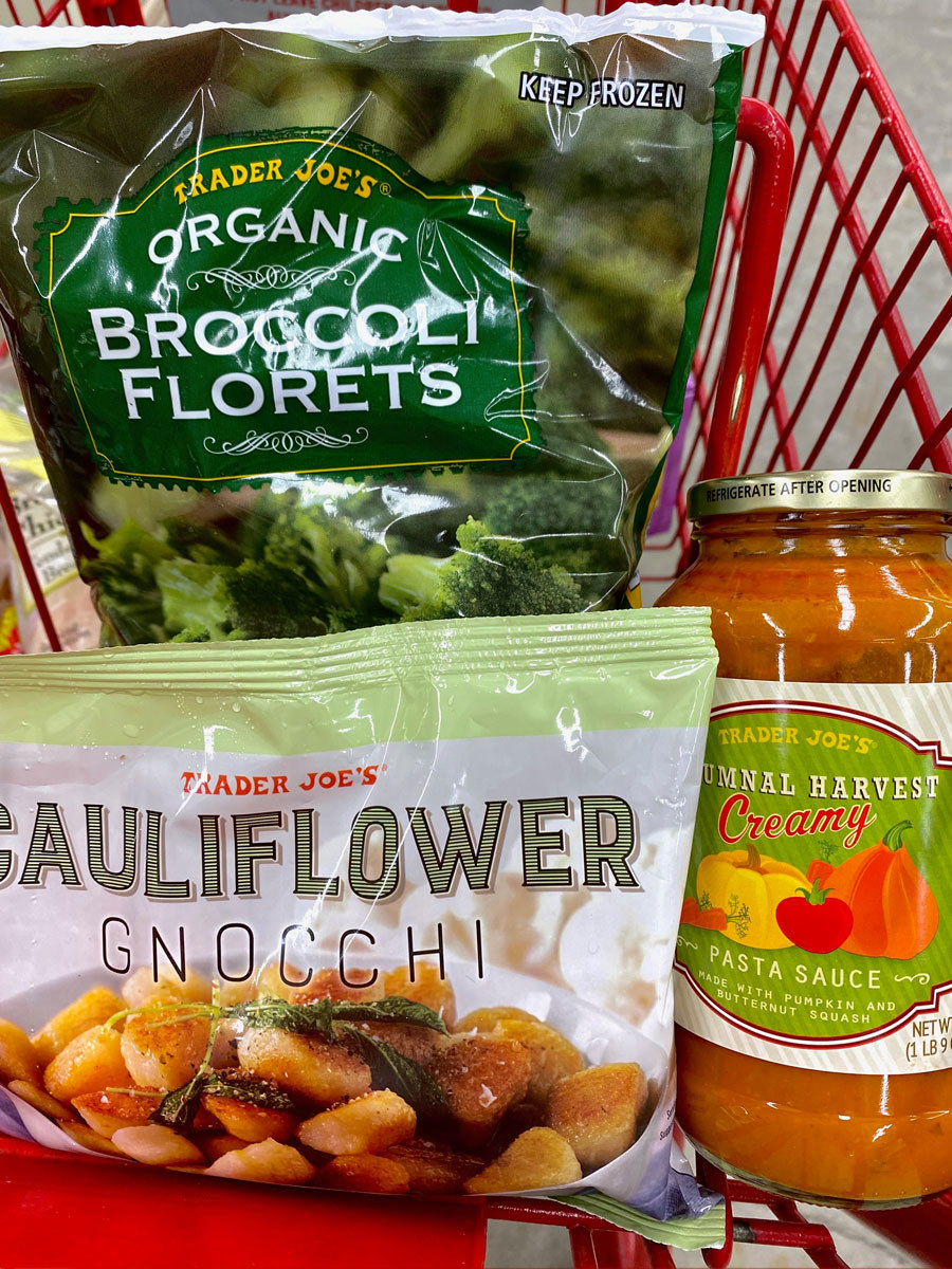 Frozen broccoli florets, cauliflower gnocchi, and a jar of autumnal harvest pasta sauce in a shopping cart.