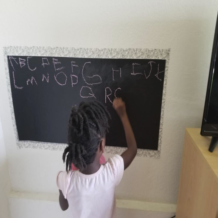 a small child writing their letters on the chalk paper which is stuck to a wall