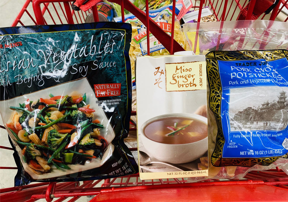 Stir fry vegetables, a carton of miso ginger soup, and frozen potstickers in a shopping cart.