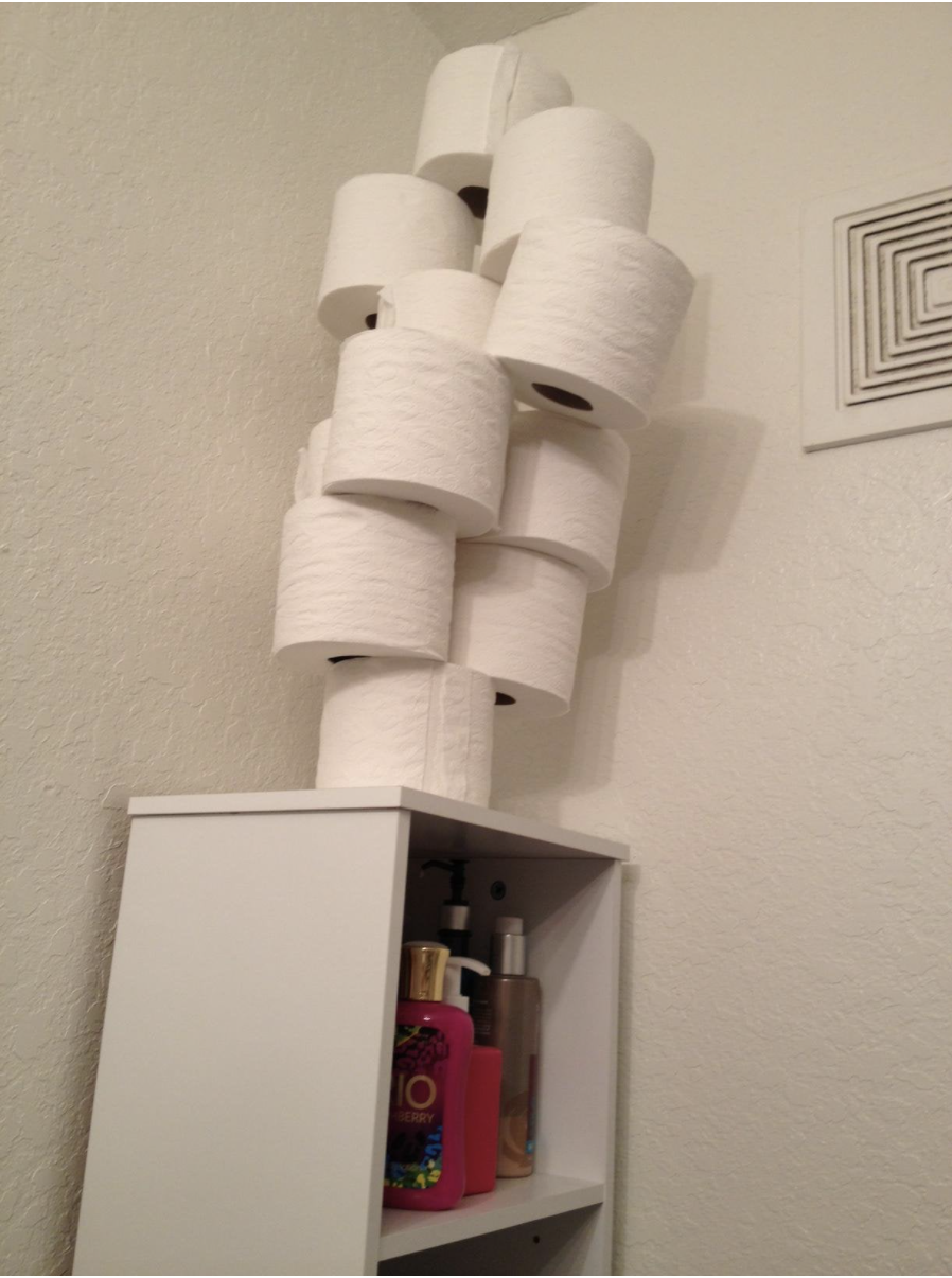 Toilet paper rolls are stacked at the very top of a bathroom shelf