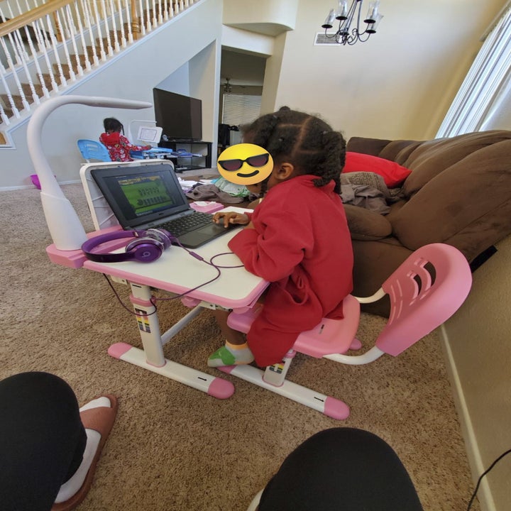 a child sitting in a pink and white chair at a pink and white desk with their laptop and headphones