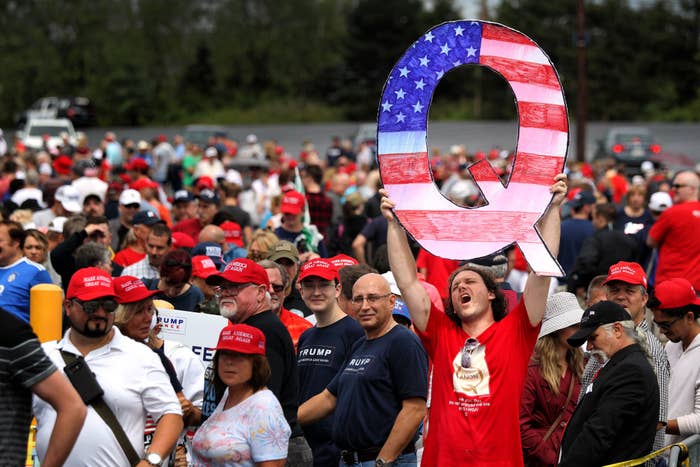 A person holds up a huge American flag–painted Q in a sea of red MAGA hats