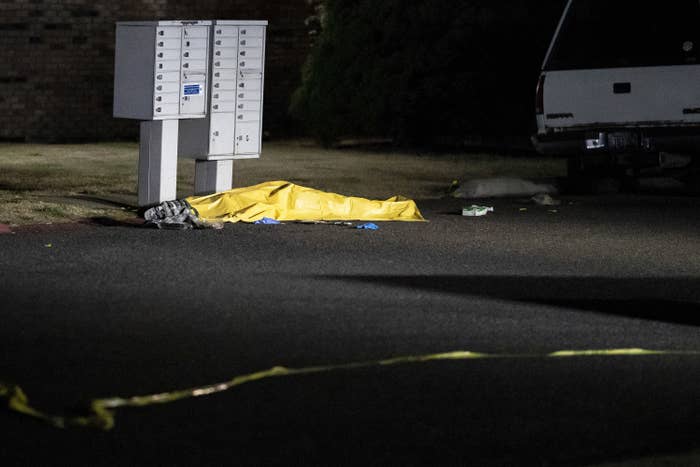 A tarpaulin covers a body as it lies next to a mailbox on a street at nighttime. 