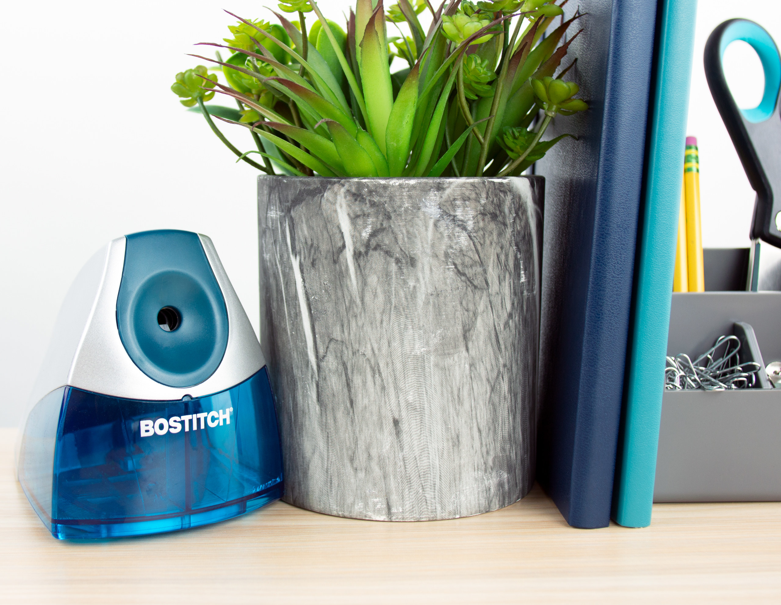 blue Bostitch electric pencil sharpener sitting on a desk next to a plant